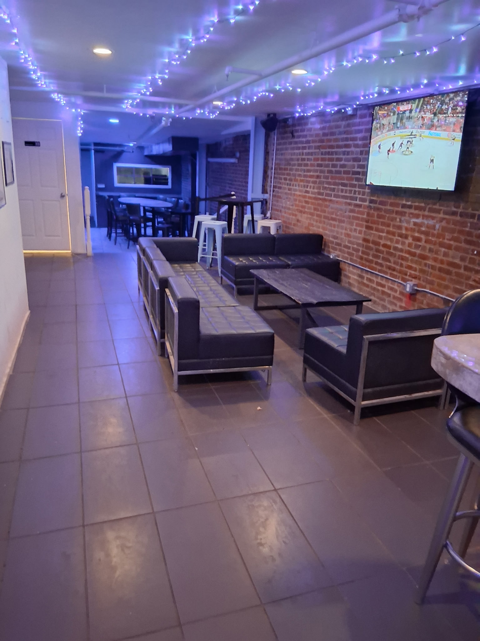 Max's Tin Can lounge area with leather couches, exposed brick, and a game on the TV